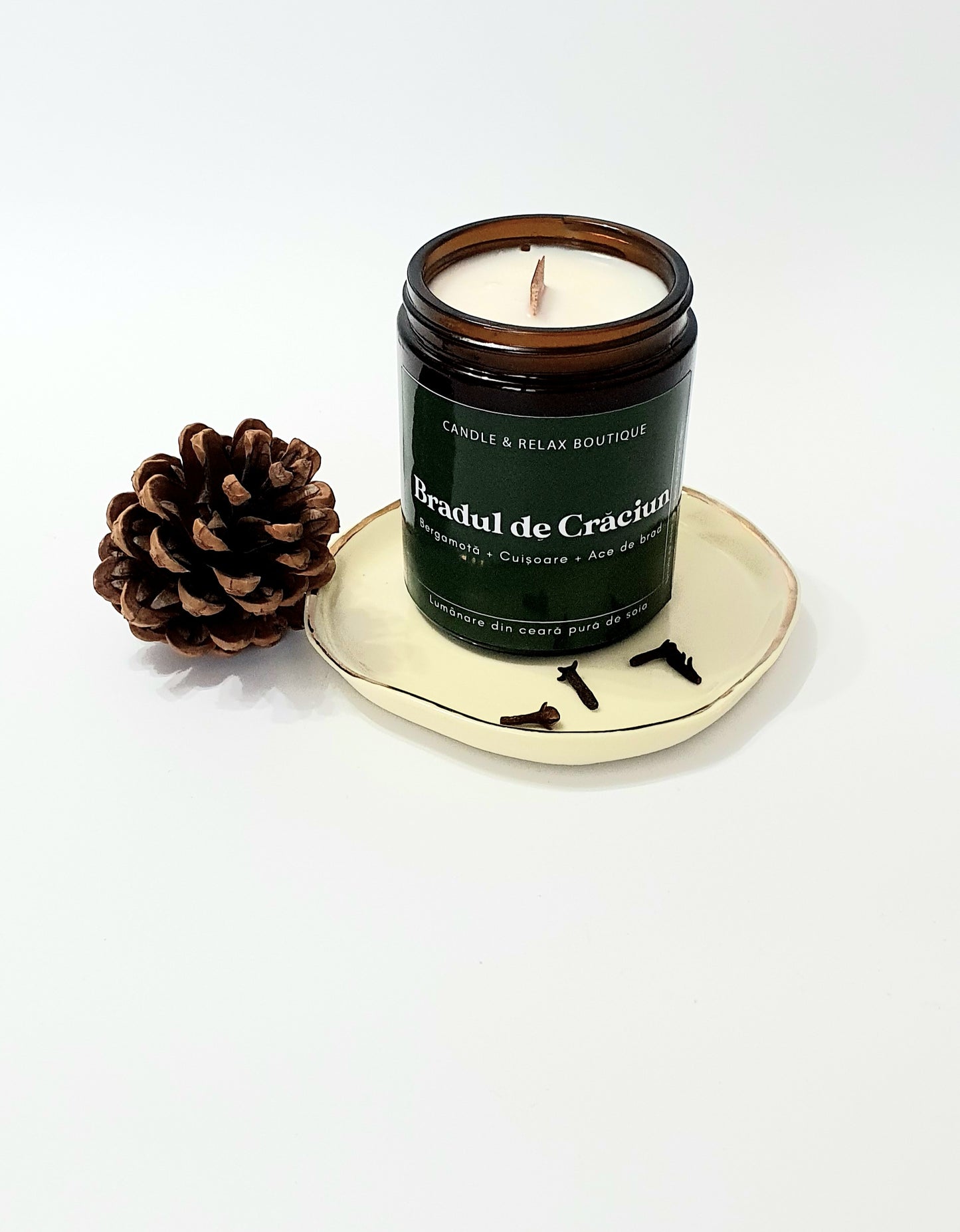 Lumanare bradul de craciun in recipient ambra pe fundal alb, con de brad, cuisoare si brad din lemn